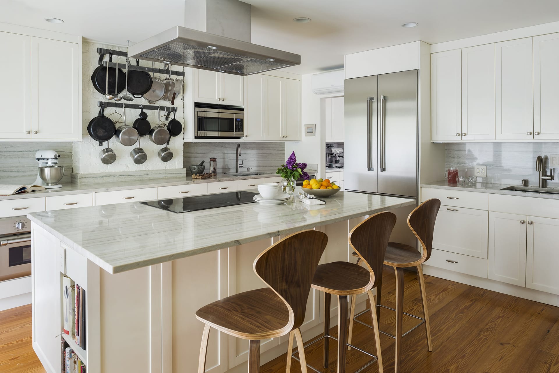 Garden-level kitchen in a Brooklyn townhouse. Range hood over the stove in the island, white millwork, brown barstools